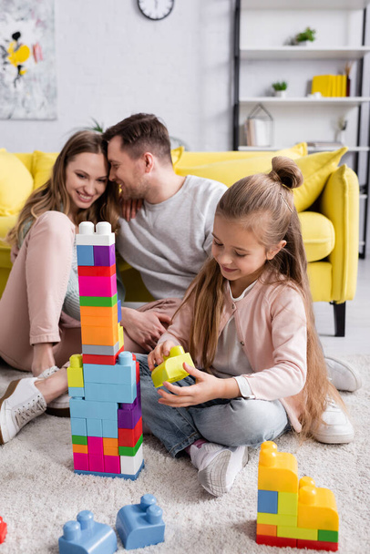 Child holding building block near parents at home  - Photo, Image