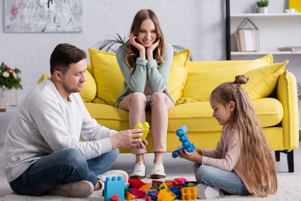 Padre e figlia giocare mattoni vicino sorridente madre sul divano  - Foto, immagini