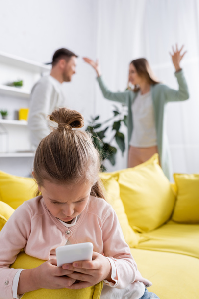 Child using smartphone while parents quarrelling at home  - Foto, immagini