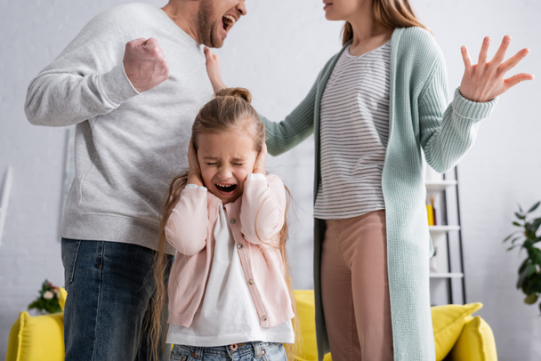 Frightened girl standing between parents quarreling  - Valokuva, kuva