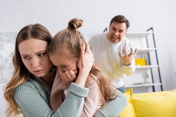 Woman hugging daughter while husband screaming on blurred background  - Фото, зображення