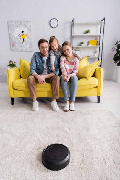 Улыбающаяся женщина указывает на роботизированный пылесос рядом с семьей  - Фото, изображение