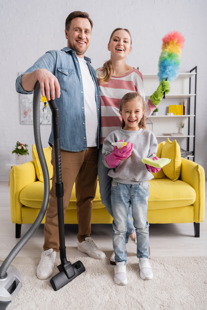 Happy family with detergent, vacuum cleaner and dust brush looking at camera  - Photo, Image