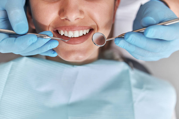 Fröhlich positive Zahnarzt und Klient in der Zahnmedizin. Patientin bei zahnärztlichen Eingriffen, Arzt mit zahnärztlichen Instrumenten in einer modernen Zahnklinik, Nahaufnahme. - Foto, Bild