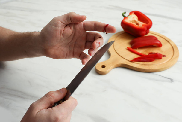 Man cut finger with knife while cooking at white marble table, closeup - Foto, imagen