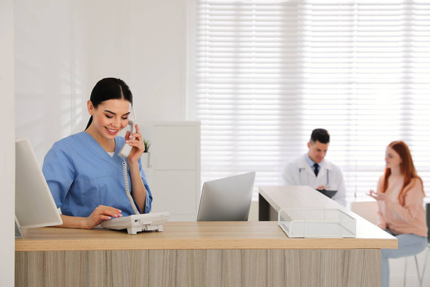 Receptionist talking on phone while doctor working with patient in hospital - Фото, изображение