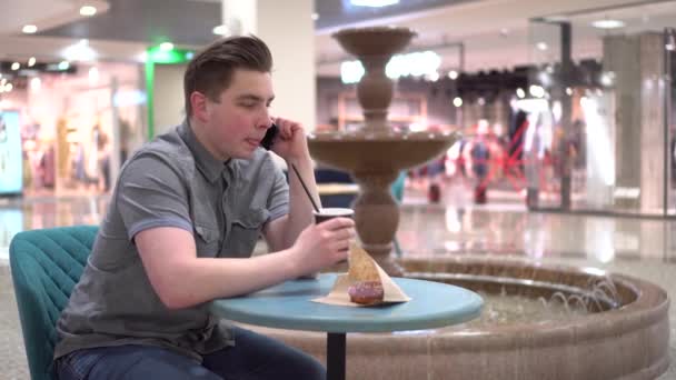 Ένας νεαρός άνδρας σε ένα καφέ μιλάει στο τηλέφωνο στο βάθος ενός σιντριβανιού. Διακόσμηση στην καφετέρια. - Πλάνα, βίντεο