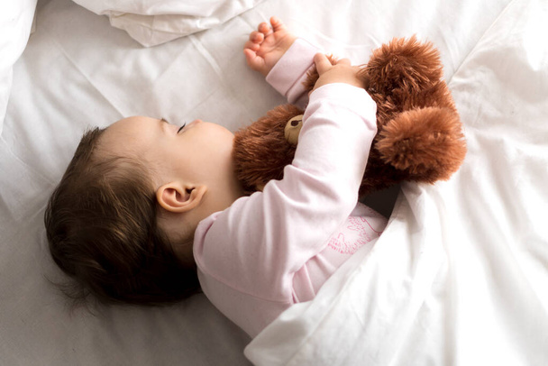 Authentic portrait cute caucasian little infant chubby baby girl or boy in pink sleep with teddy bear on white bed. child resting at lunchtime. care, Sleeping kid, Childhood, Parenthood, life concept - Fotografie, Obrázek