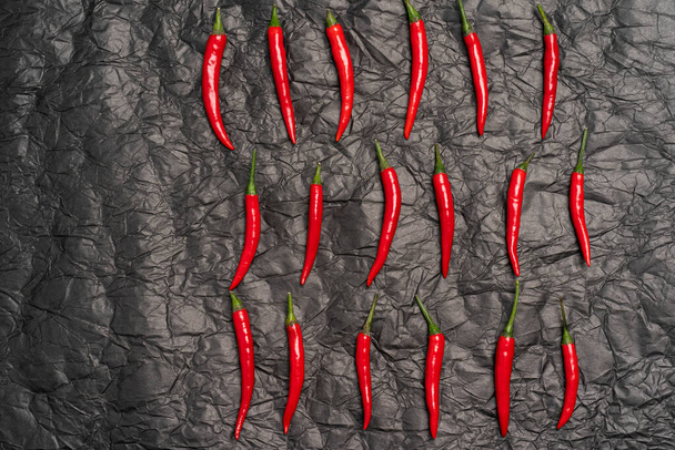 Κόκκινο ζεστό chili πιπεριές μοτίβο σε μαύρο τσαλακωμένο φόντο υφή, top view φόντο με αντίγραφο χώρο - Φωτογραφία, εικόνα