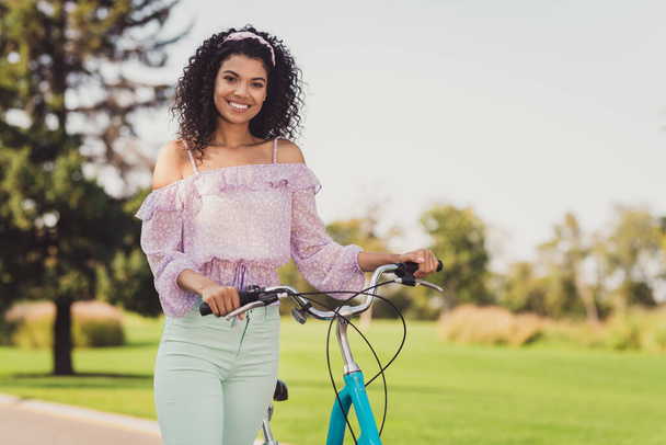 Photo of optimistic brunette lady stand with bicycle wear lilac top pants outside walk in park - 写真・画像