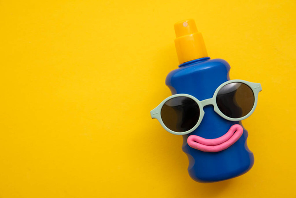 Happy sun block bottle wearing sunglasses and a smile on a yellow background - Foto, Imagen