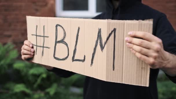 仮面の男は手に段ボールポスターで立つ – BLACK LIVES MATTER - 映像、動画