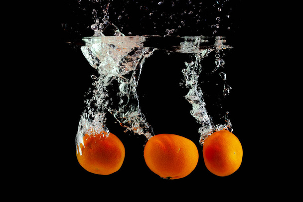 three fresh tangerines fell into the water with splashes - Photo, Image