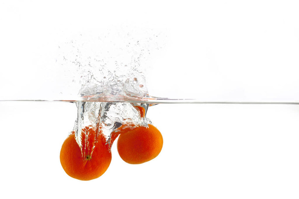 two ripe orange tangerine falls into the water with splashes on a white background, isolate - Photo, Image
