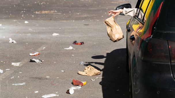 Nainen, joka pitelee roskapussia kädessään, ulos ikkunasta ajaen autolla. Kuljettaja heittää roskia pysäköintiin. Ympäristön pilaantuminen - Valokuva, kuva
