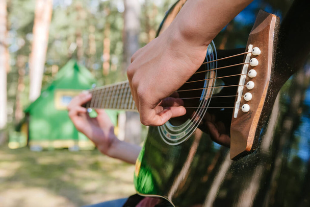 Close-up of a guy playing the guitar. Against the background of a forest and a house in nature - Фото, зображення