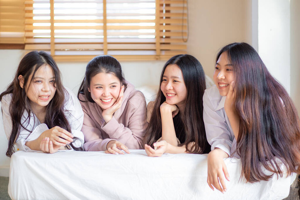 ベッドの上に横たわる4人のアジア人女性のグループ笑顔カメラを見て幸せな友人や十代の女の子を感じます楽しいです家の中で居心地の良い部屋 - 写真・画像
