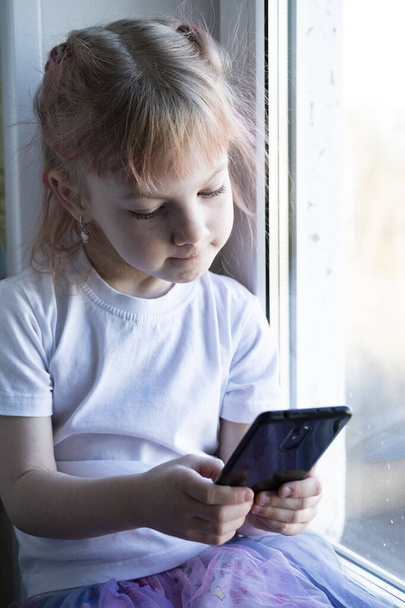 dítě sedí na parapetu a hraje si s chytrým telefonem - Fotografie, Obrázek