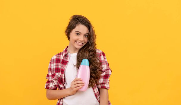 ευτυχισμένη έφηβος κορίτσι με μακριά σγουρά μαλλιά κρατήστε μπουκάλι σαμπουάν, καλλυντικά. - Φωτογραφία, εικόνα