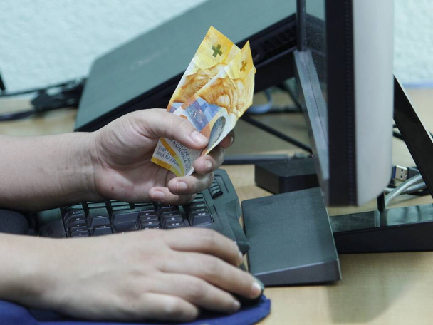handen van een vrouw met Zwitsers geld op een toetsenbord - Foto, afbeelding