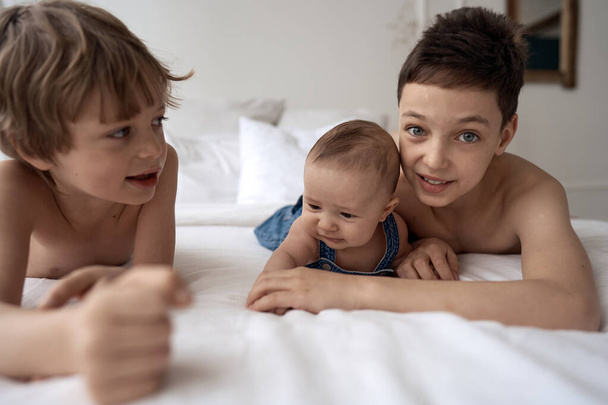 Three funny brothers boys are lying on the bed and having fun - Фото, зображення