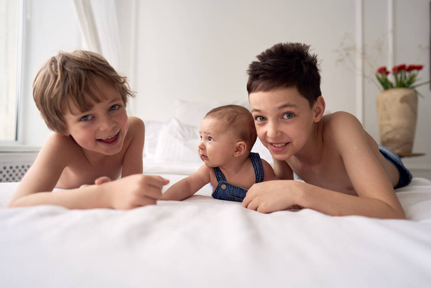 Three funny brothers boys are lying on the bed and having fun - Fotografie, Obrázek