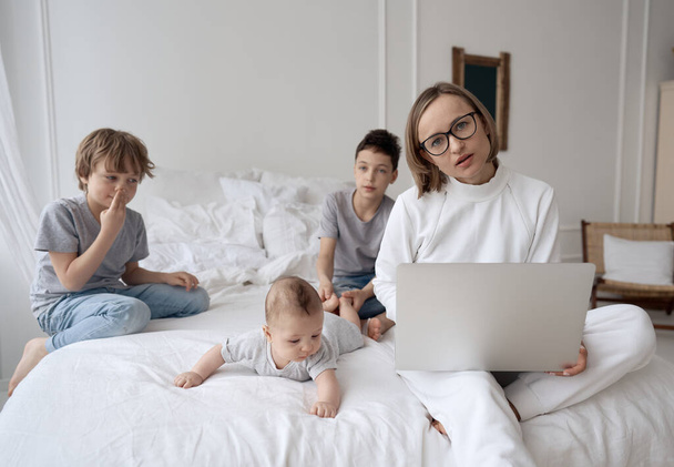 Busy caucasian woman trying to work while baby sitting three kids. Caucasian single mom work from home with the children. - Photo, image