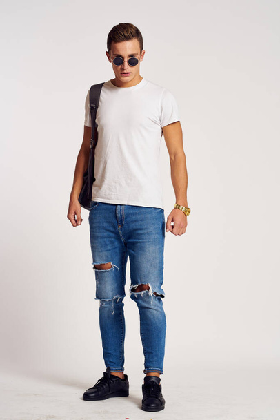 a man with a backpack on his back in jeans t-shirt full length sneakers and glasses on his face - Foto, afbeelding