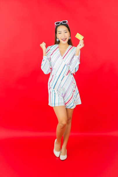 Retrato hermosa joven mujer asiática con tarjeta de crédito y bolsa de compras en fondo de color rojo - Foto, imagen