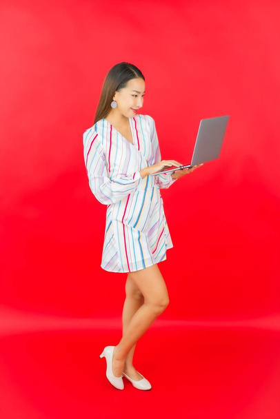Portrait belle jeune femme asiatique utiliser ordinateur portable pour le travail sur fond rouge - Photo, image