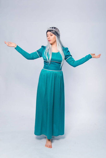 Full length portrait of a princess in a medieval, fantasy, turquoise dress with ash hair and a silver crown, posing isolated on a white background. - Фото, изображение
