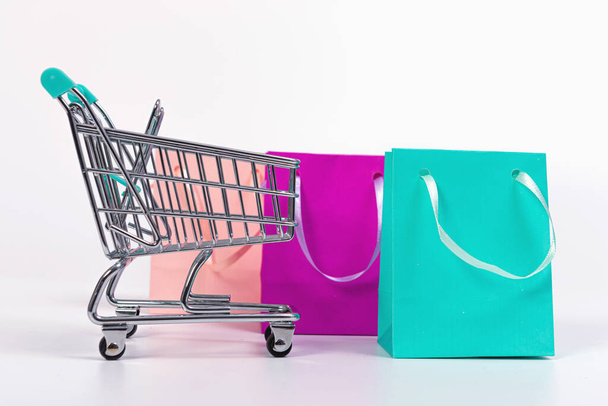 empty mini shopping cart and colourful paper bags isolated on light background, mockup for design - Foto, imagen