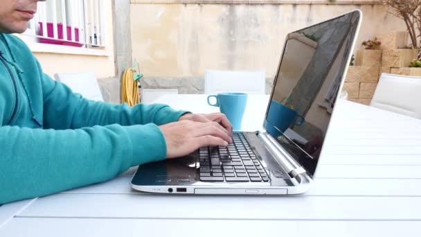 Junger Mann telefoniert, tippt auf seinem Laptop im Garten seines Hauses - Filmmaterial, Video
