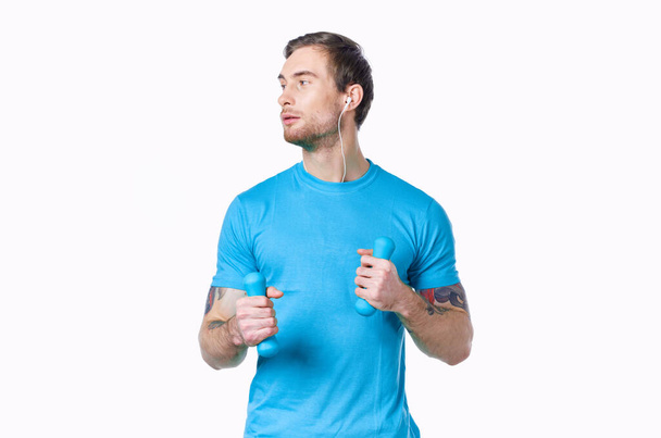 man with dumbbells in a blue t-shirt on a light background looking to the side cropped view - Photo, Image
