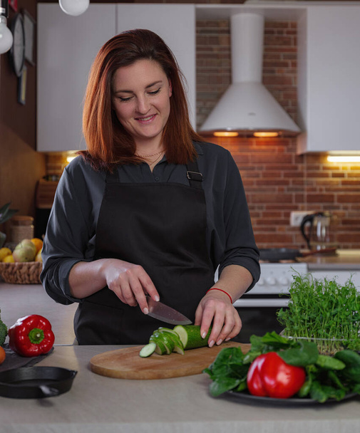 Концепция здорового питания портрет красивой молодой рыжеволосой женщины, которая готовит вкусную еду, режет овощи для приготовления пищи - Фото, изображение
