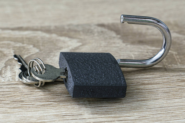 an open lock with keys in the keyhole on a wooden surface. High quality photo - Photo, Image