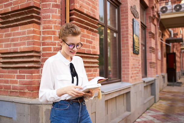 indignant woman with book near brick building of education institute retro style - Photo, Image