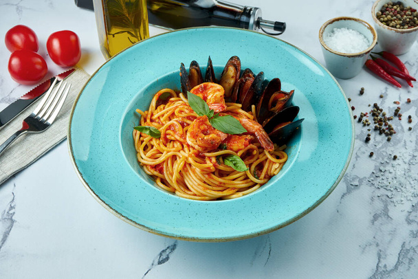 Appetizing Italian pasta with tiger prawns, tomato sauce, Chilean mussels in a blue plate on a marble background. Spaghetti with seafood - Foto, imagen