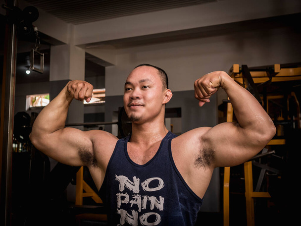 Ein großer, stämmiger Mann posiert in der Turnhalle mit einem doppelten Bizeps. Bodybuilding-Subkultur. - Foto, Bild
