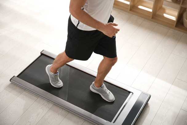 Sporty man training on walking treadmill at home, closeup - Photo, Image