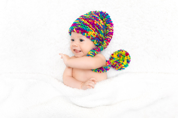 Novorozené dítě ležící na bílé přikrývce ve velkém legračním pleteném klobouku. Adopční koncept, šťastné rodičovství - Fotografie, Obrázek