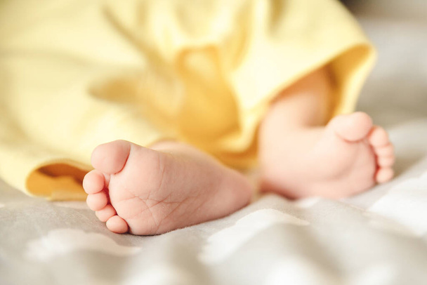 Foto von kleinen Babyfüßen, die in gelbes Handtuch gewickelt sind. Fusshaut-Pflegekonzept, Nahaufnahme von winzigen Barfüßlern - Foto, Bild