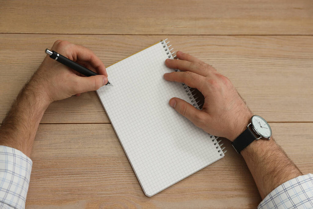 Left-handed man writing in notebook at wooden table, top view - Фото, изображение