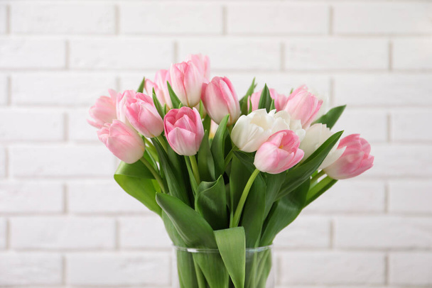 Beautiful bouquet of tulips in glass vase against white brick wall - Foto, immagini