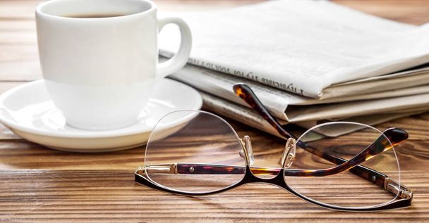 Eyeglasses with newspapers and cup of coffee on the table. - Фото, зображення