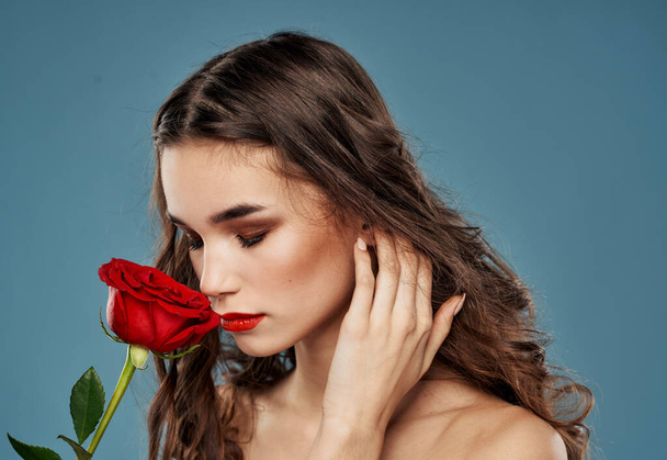 Retrato de uma mulher bonita com uma flor vermelha em um fundo azul e modelo de maquiagem à noite - Foto, Imagem