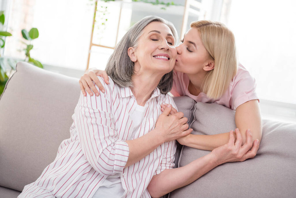 Photo of happy mother and daughter good mood sit sofa kiss cheek trust care indoors inside house home flat - Foto, immagini