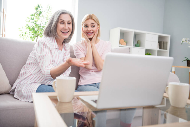 Photo of happy excited cheerful mom and daughter sit couch look laptop movie indoors inside house home - Фото, зображення