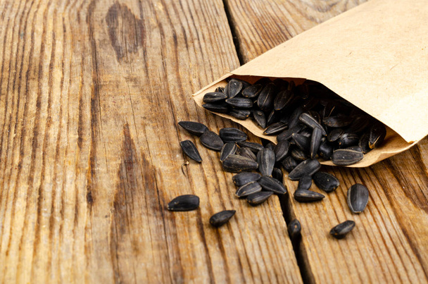 Black unpeeled sunflower seeds in craft bag on wooden table. Studio Photo - Photo, Image