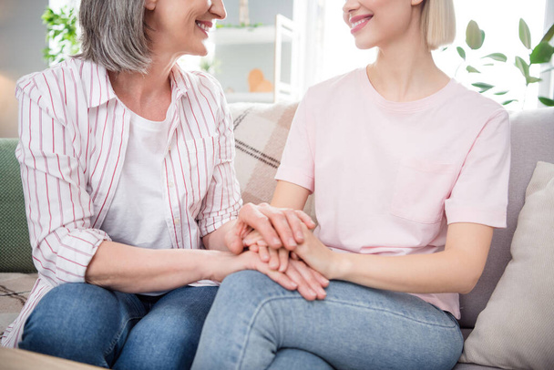 Cropped photo of young woman and old lady family sit sofa hold hands good mood indoors inside house home - Foto, immagini